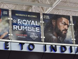 Several graphics of WWE Superstars hang above on a bridge at the airport. This photo shows the "WWE Royal Rumble 2025" logo and Roman Reigns.