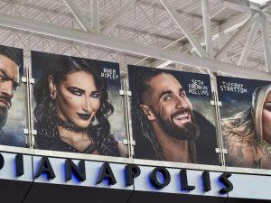 Several graphics of WWE Superstars hang above on a bridge at the airport. This photo shows Roman Reigns, Rhea Ripley, Seth Rollins, and Tiffany Stratton.