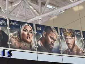 Several graphics of WWE Superstars hang above on a bridge at the airport. This photo shows Tiffany Stratton, Solo Sikoa, and Logan Paul.