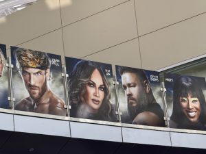 Several graphics of WWE Superstars hang above on a bridge at the airport. This photo shows Logan Paul, Nia Jax, Kevin Owens, and Naomi.