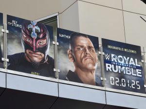 Several graphics of WWE Superstars hang above on a bridge at the airport. This photo shows Rey Mysterio, Gunther, and the "WWE Royal Rumble 2025" logo.