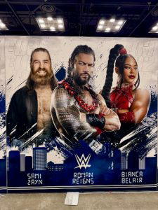 A graphic of Sami Zayn, "The Original Tribal Chief" Roman Reigns, and "The EST of the WWE" Bianca Belair.