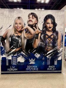 A graphic of Liv Morgan, "Dirty" Dominik Mysterio, and "Mami" Rhea Ripley.